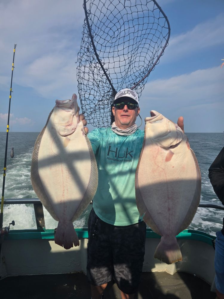 Person on boat holding two large fish with a net in the background.