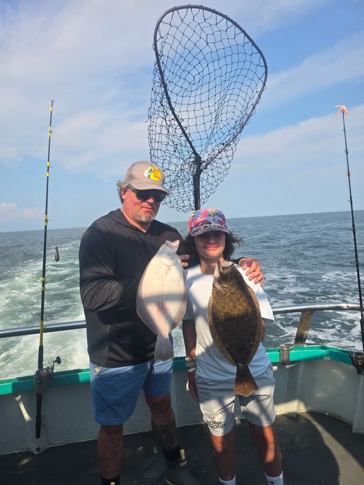 Two people on a boat holding fish with a fishing net in the background.