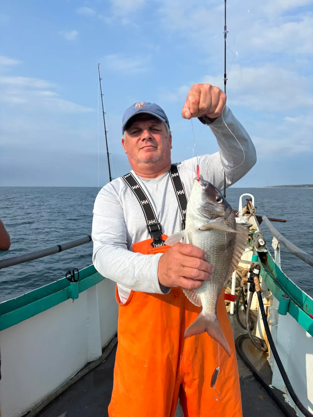 Man on boat holding a fish with ocean in the background.