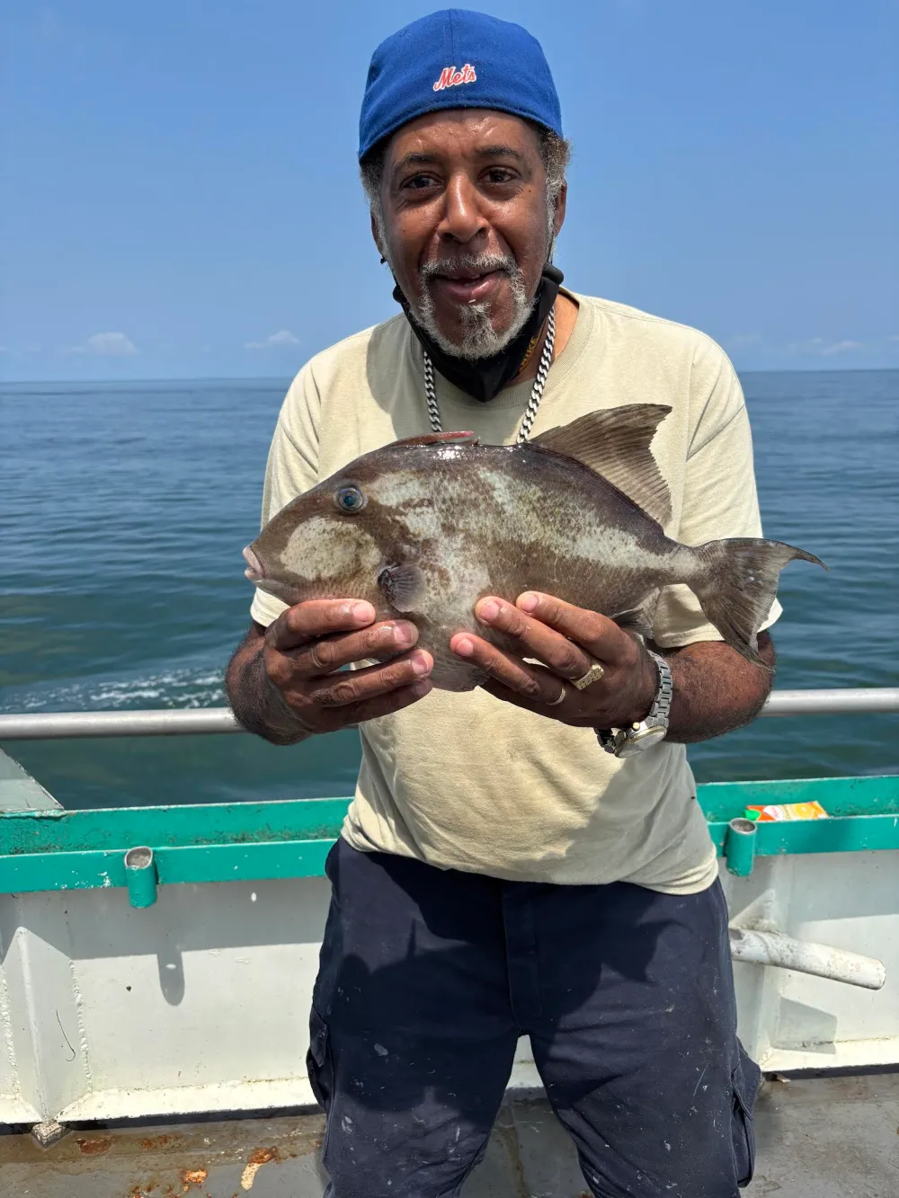 Man on boat holding a fish in front of a calm ocean.