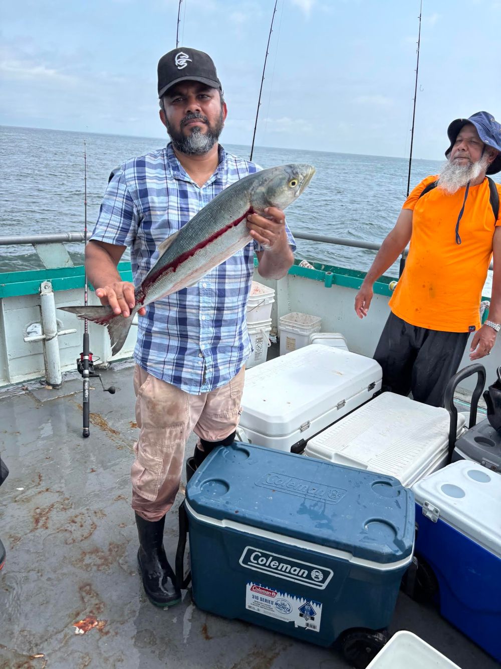 Man holding a fish on a boat with coolers and fishing rods.