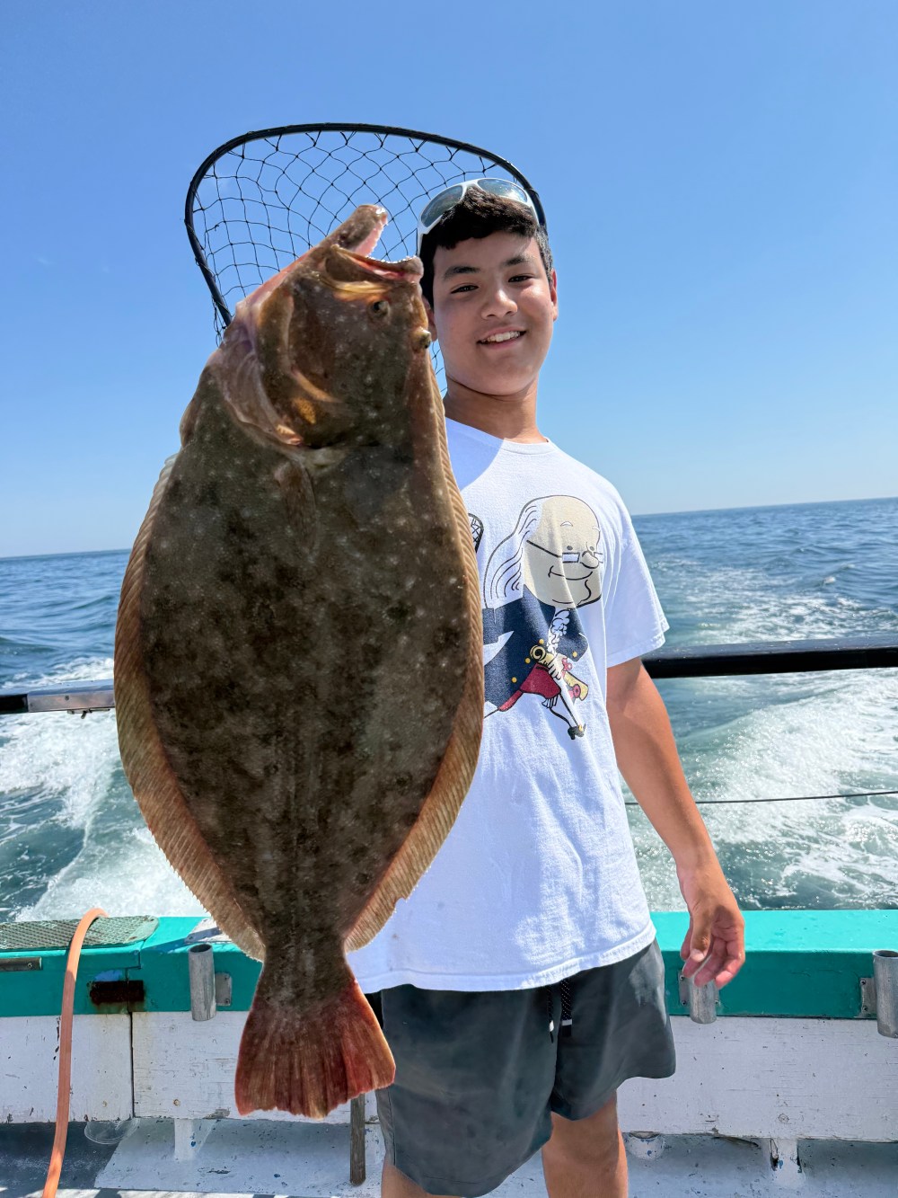 Person holding a large fish with a net on a boat at sea.