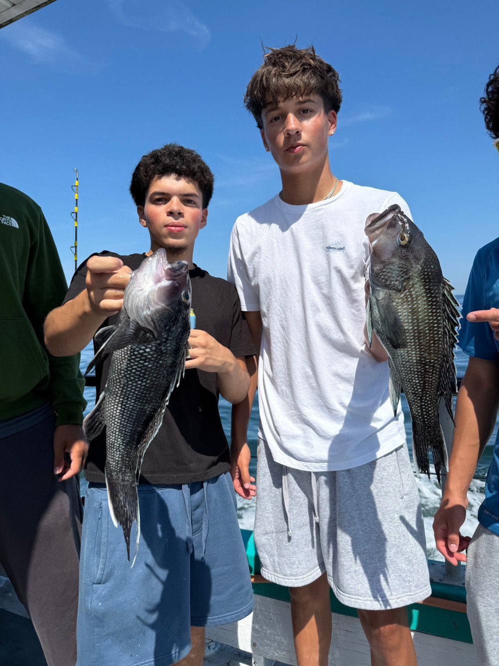 Two people holding fish on a boat with blue sky background.