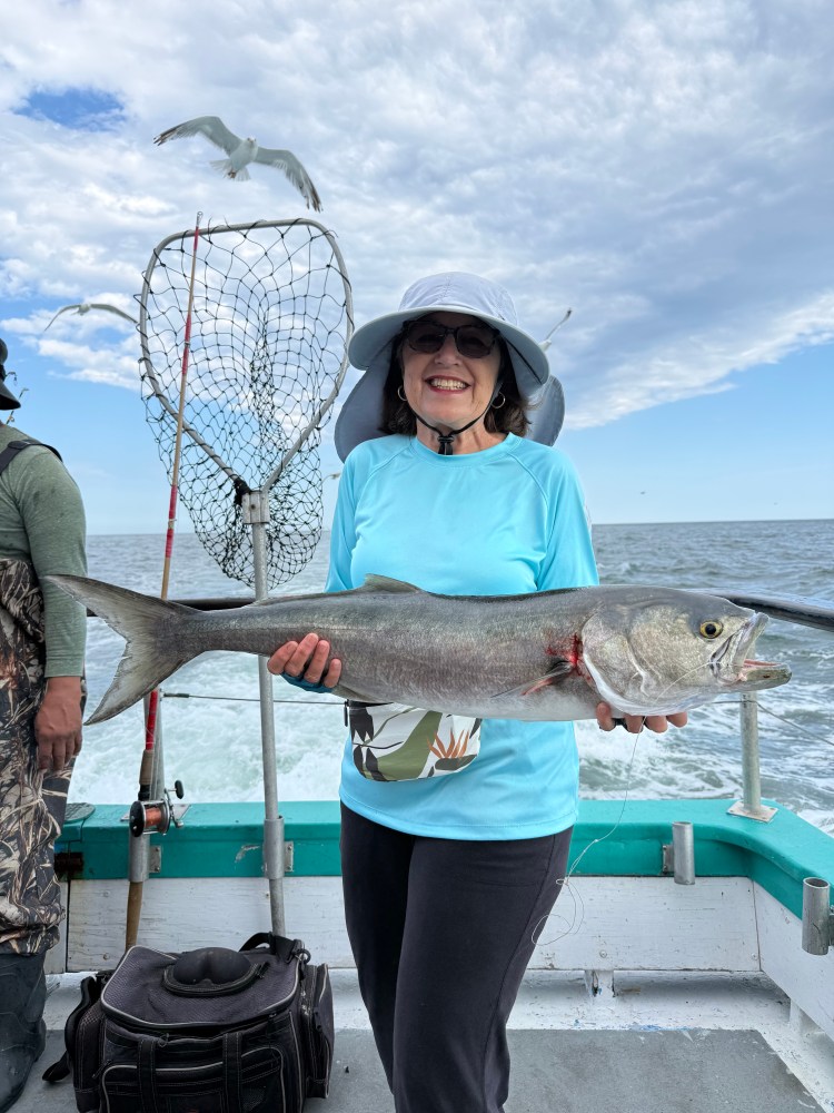 Smiling woman on boat holding a large fish, with a seagull and net in the background.