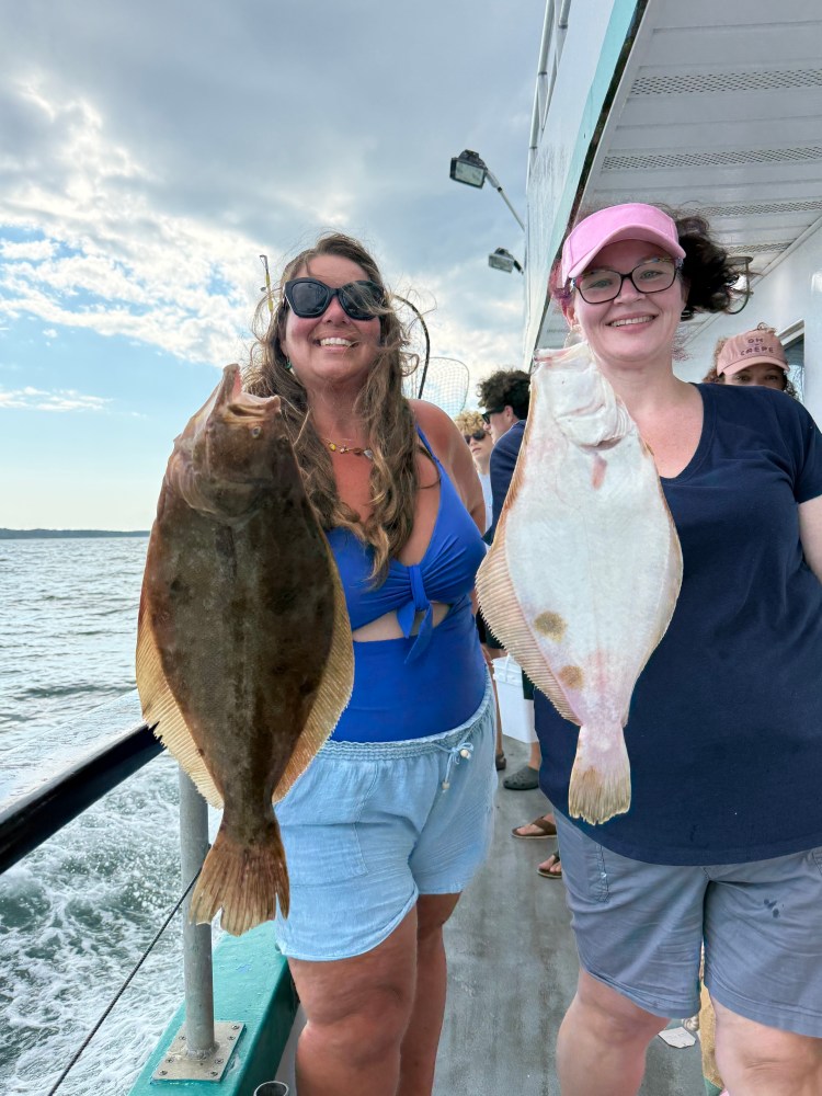 Two women smiling on a boat holding large flat fish.