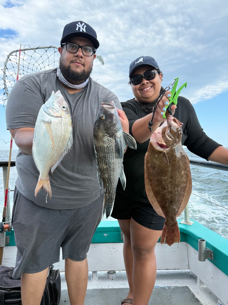 Two people holding fish on a boat with a fishing net in the background.