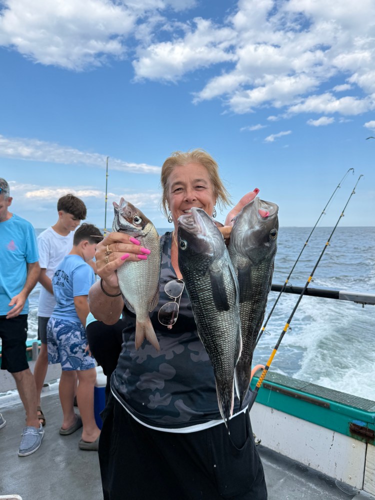 Woman holding three fish on a boat with ocean and people in background.