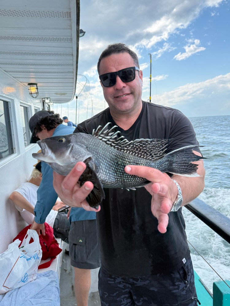 Man holding a fish on a boat with ocean in background.