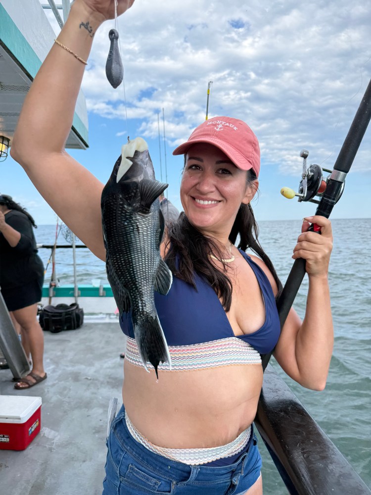 Woman in a cap holding a fish on a boat, smiling.
