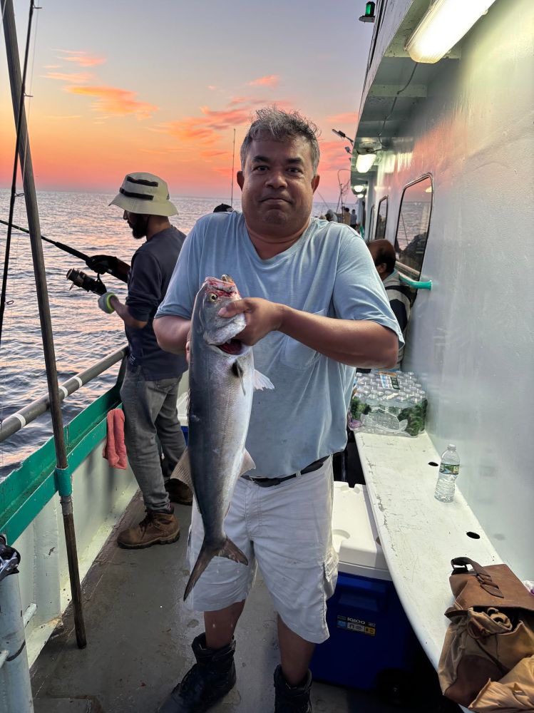 Man holding a fish on a boat at sunset with others fishing in the background.