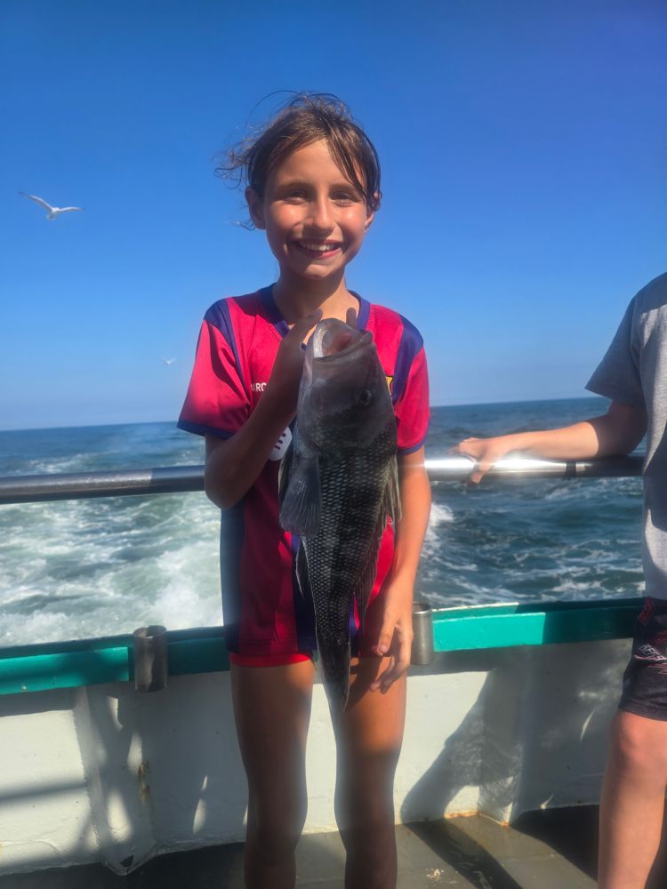 Smiling child holding a fish on a boat with ocean background.