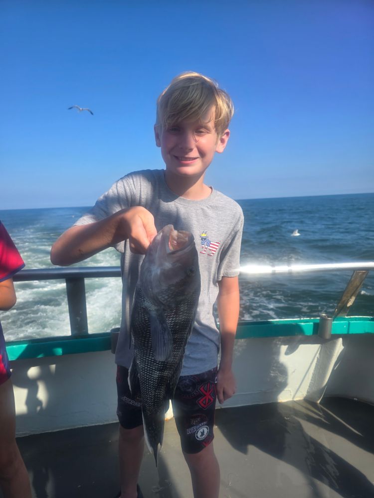 Child holding a fish on a boat with ocean in the background.