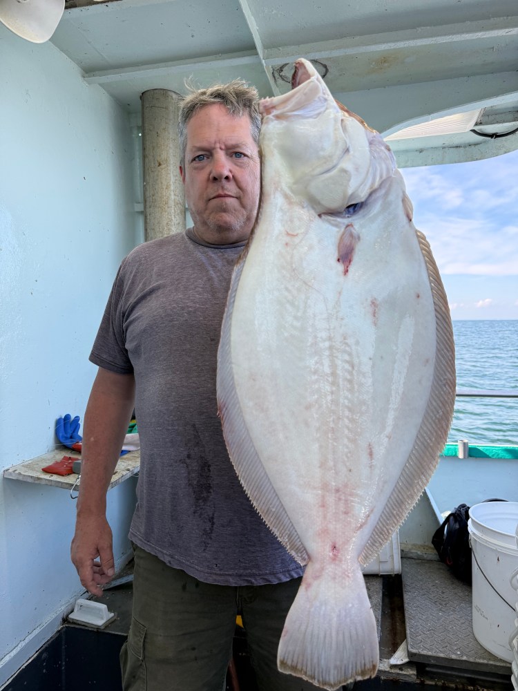 Man holding a large flat fish on a boat with ocean background.