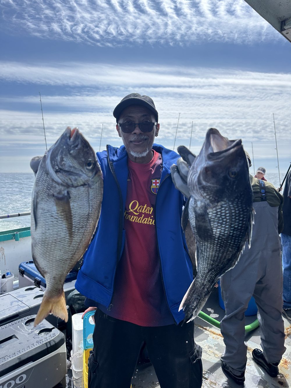 Person holding two large fish on a boat under a cloudy sky.
