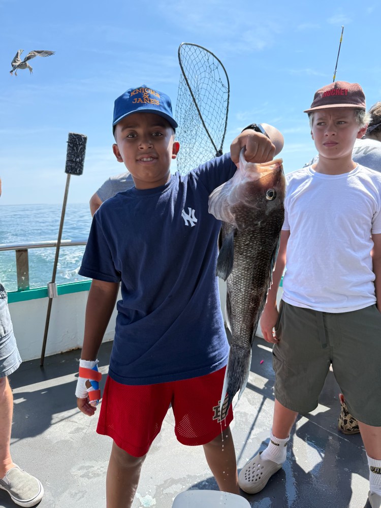 Boy holding large fish on a boat, with another boy and a net in the background.