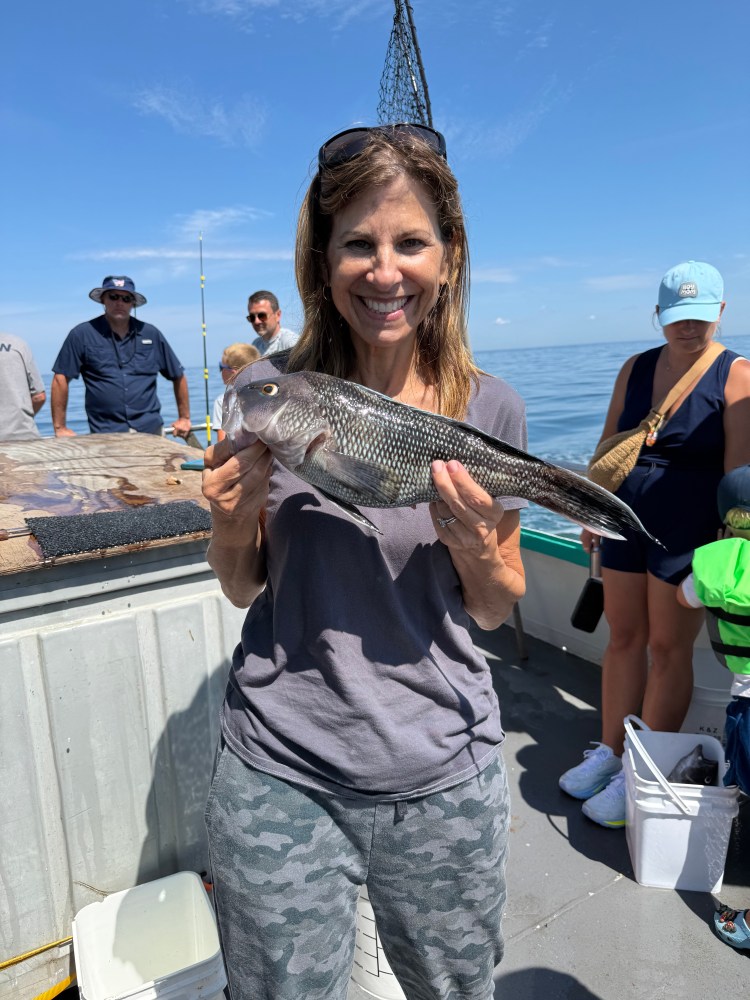 Woman holding a fish on a boat with people and ocean in background.