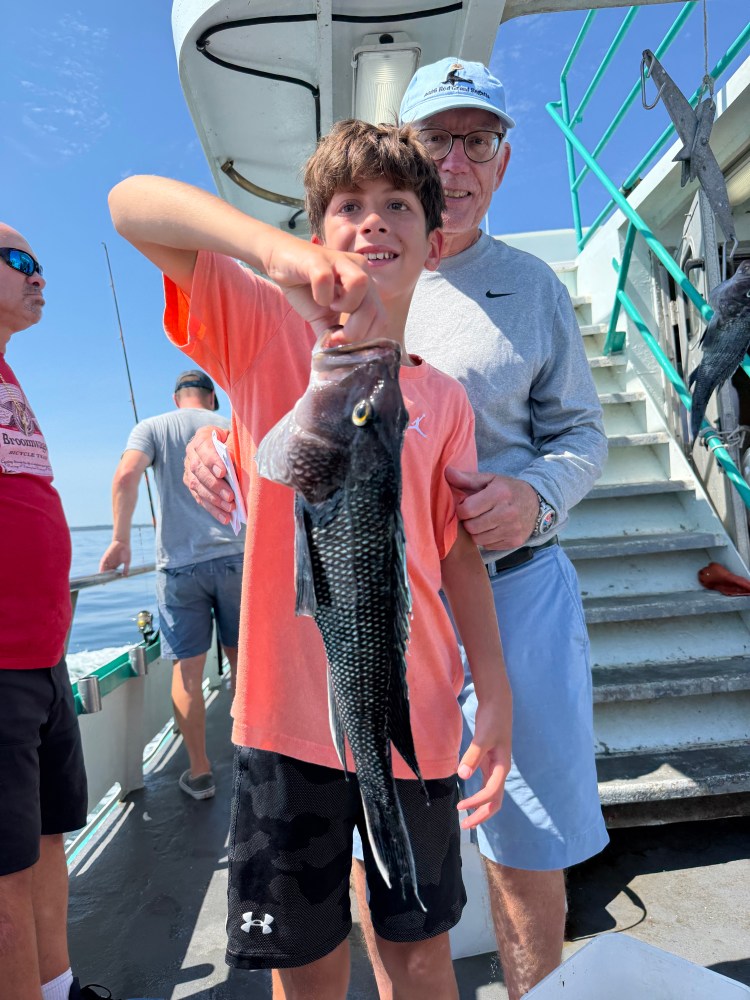 Boy holding a fish on a boat, with an older man beside him.