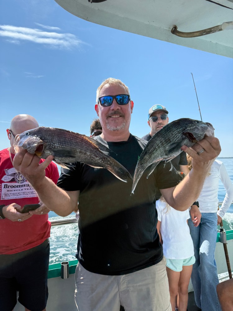 Man holding two fish on a boat with people in the background.