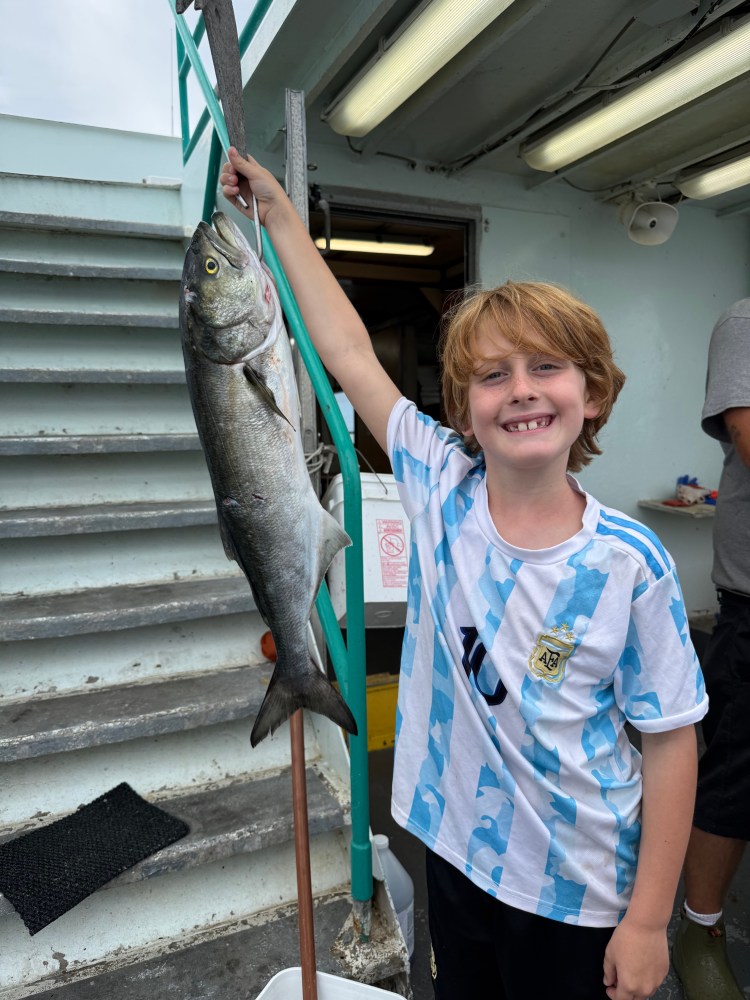 Smiling child holding a large fish on a boat.