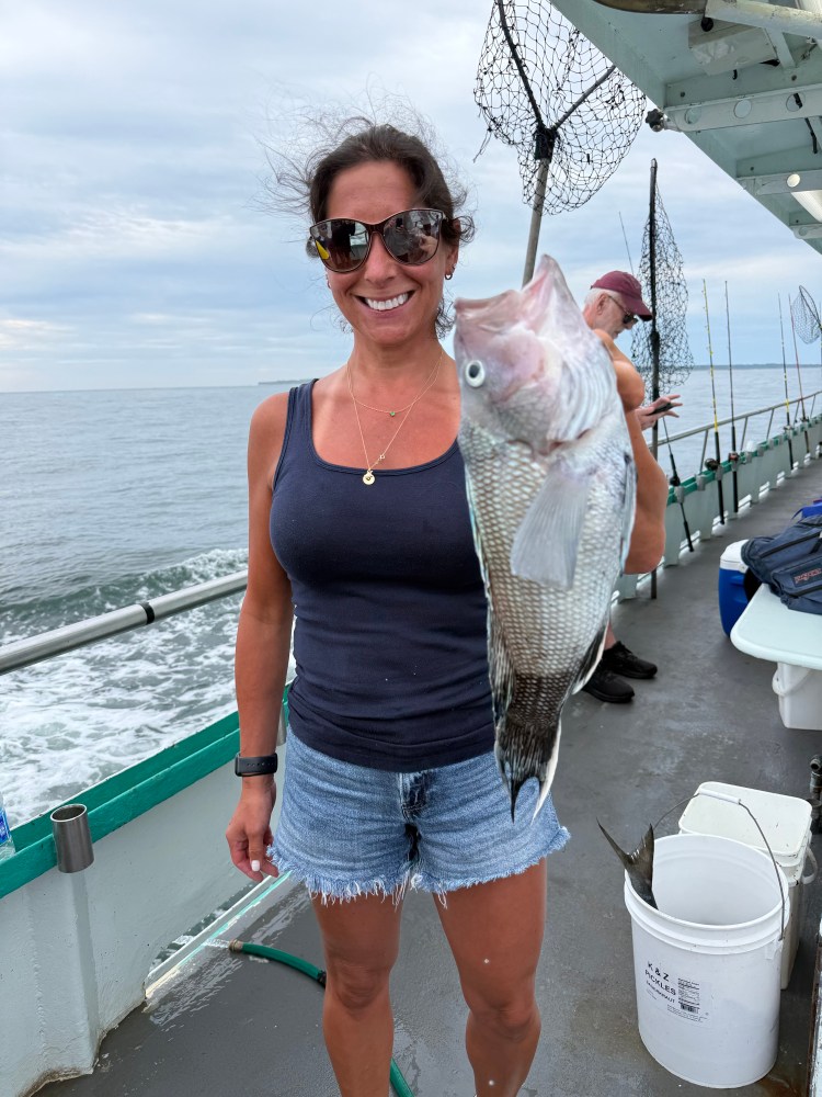 Woman holding a large fish on a boat with fishing nets.