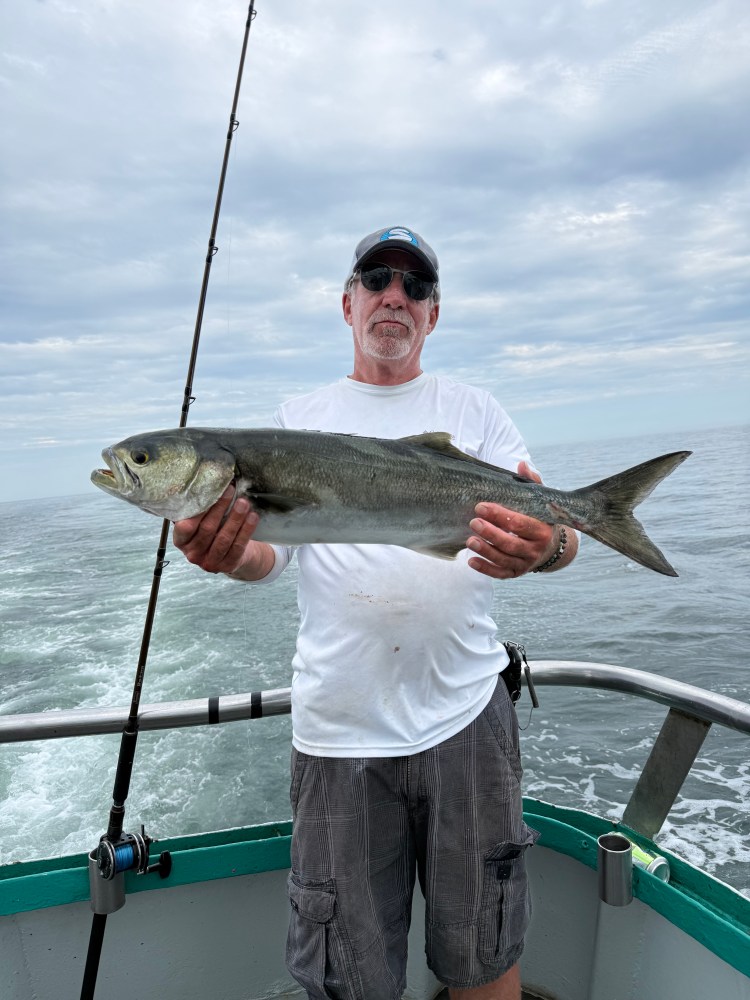 Man holding a large fish on a boat under a cloudy sky.