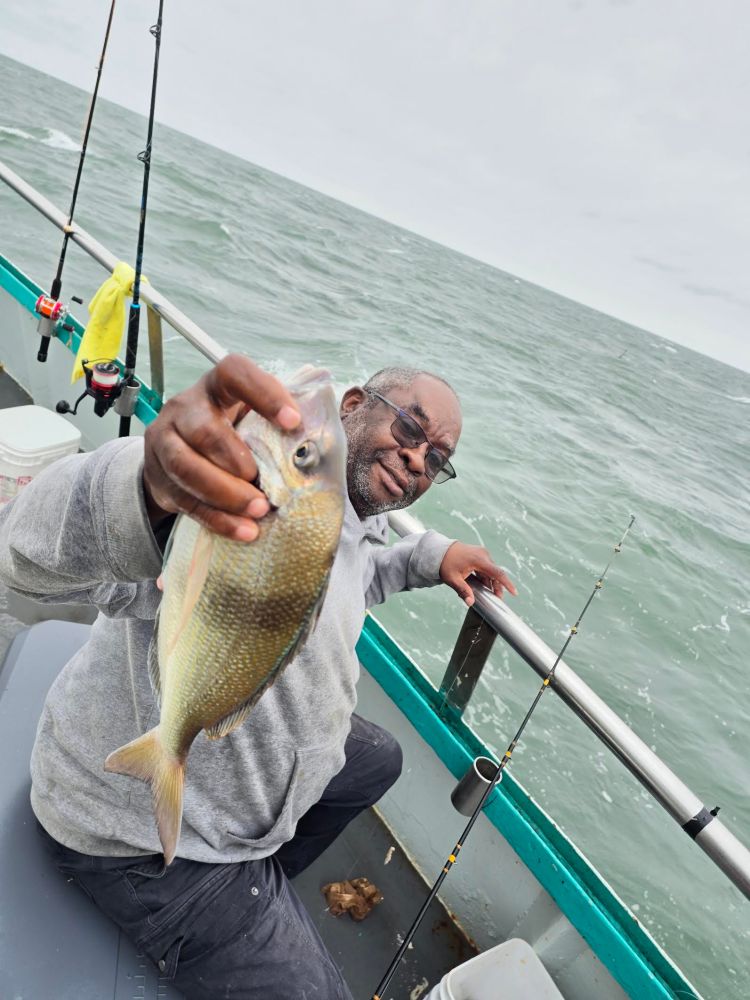 Man on a boat holding a fish with ocean in the background.