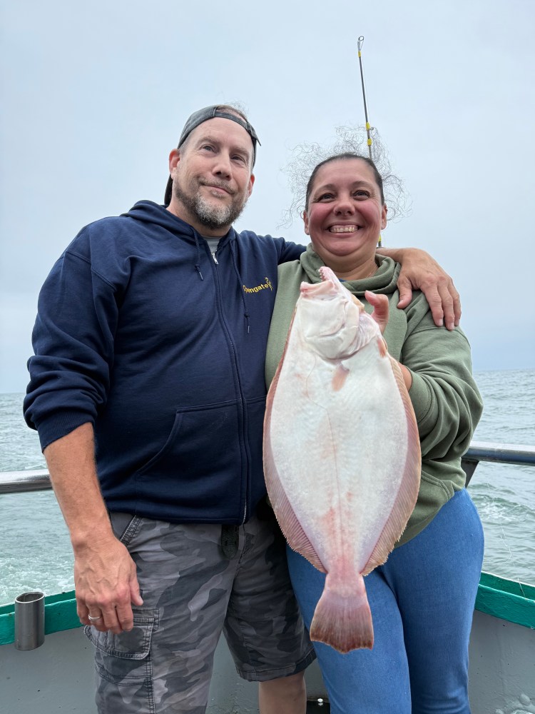 Smiling man and woman on a boat holding a large fish.