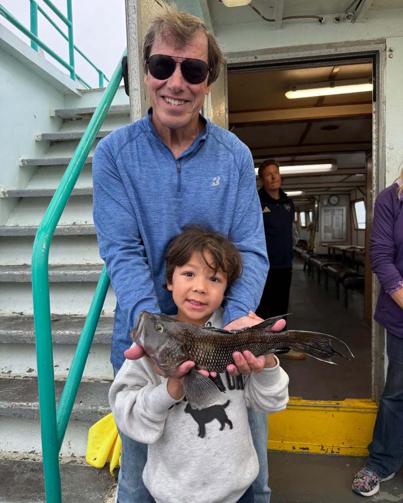 Man and child proudly holding a large fish on a boat.
