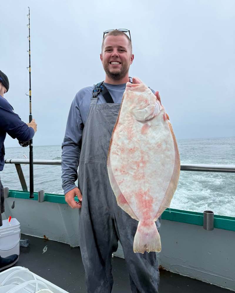 Person holding a large flat fish on a boat, ocean in background.