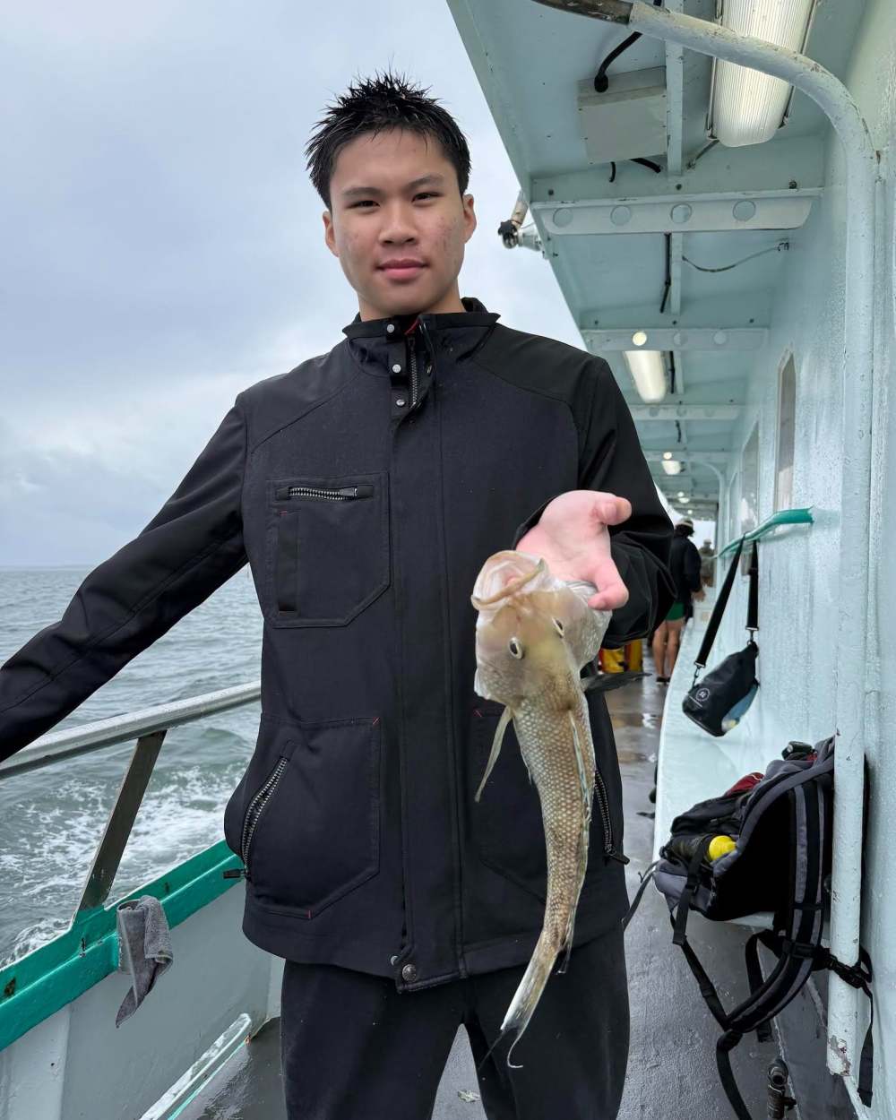 Person holding a fish on a boat, cloudy sky in the background.