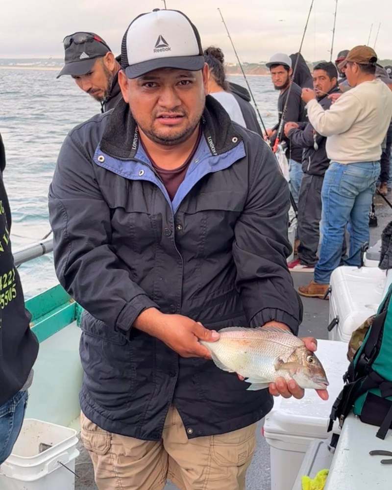 Man holding fish on a boat with several people fishing.