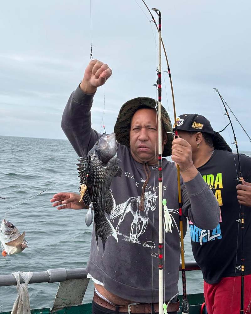 Two people on a boat holding fishing rods with fish caught.