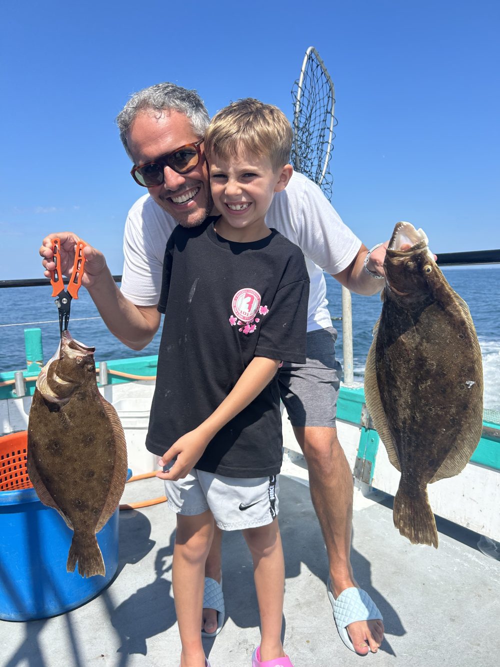 Adult and child holding fish on a boat under a clear blue sky.