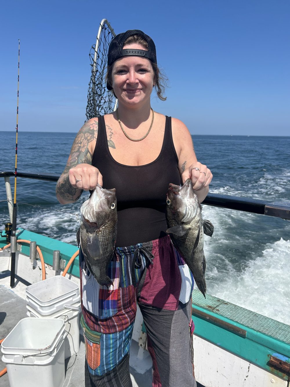 Person holding two fish on a boat with ocean in the background.