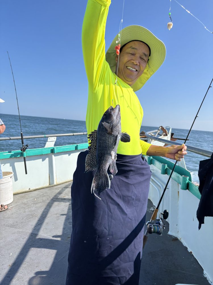 Person in a bright shirt on a boat holding a caught fish, smiling.