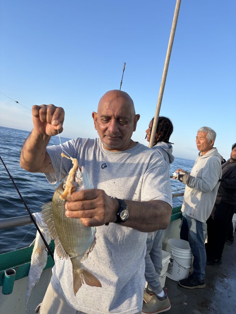 Man holding a fish on a boat with others in background under a clear sky.
