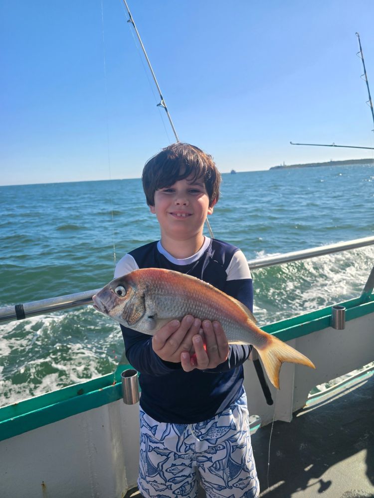Child on a boat holding a fish, with the ocean in the background.