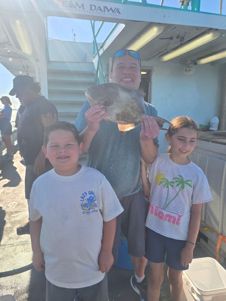Two children and a man holding a fish on a boat, sunny day.