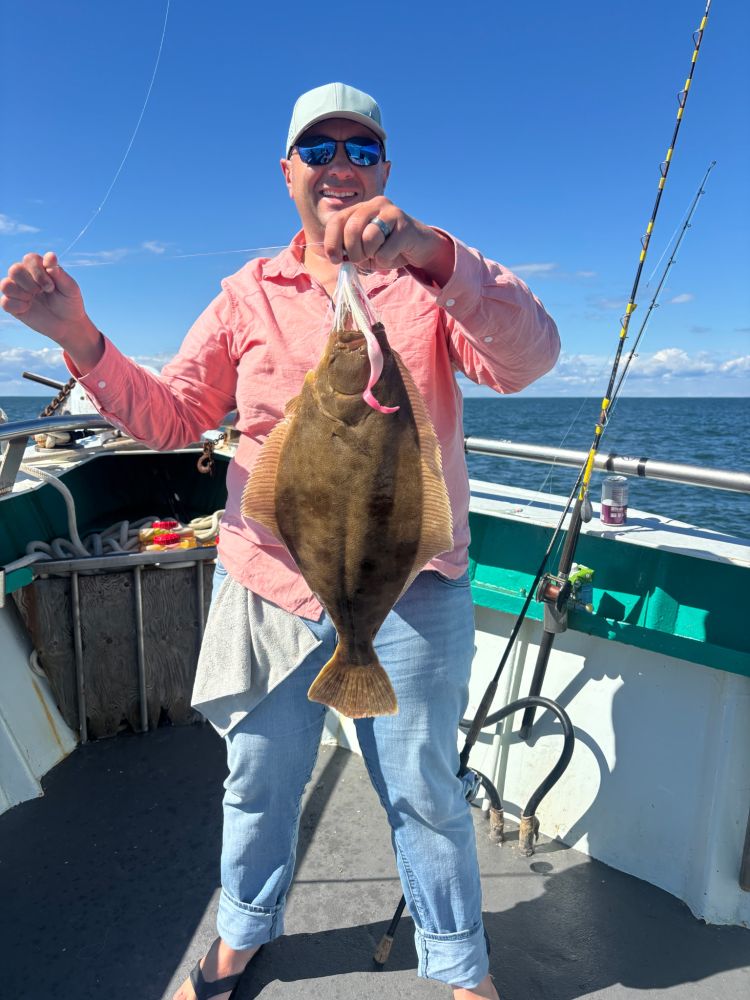 Person on a boat holding a large flat fish, wearing a cap and sunglasses.