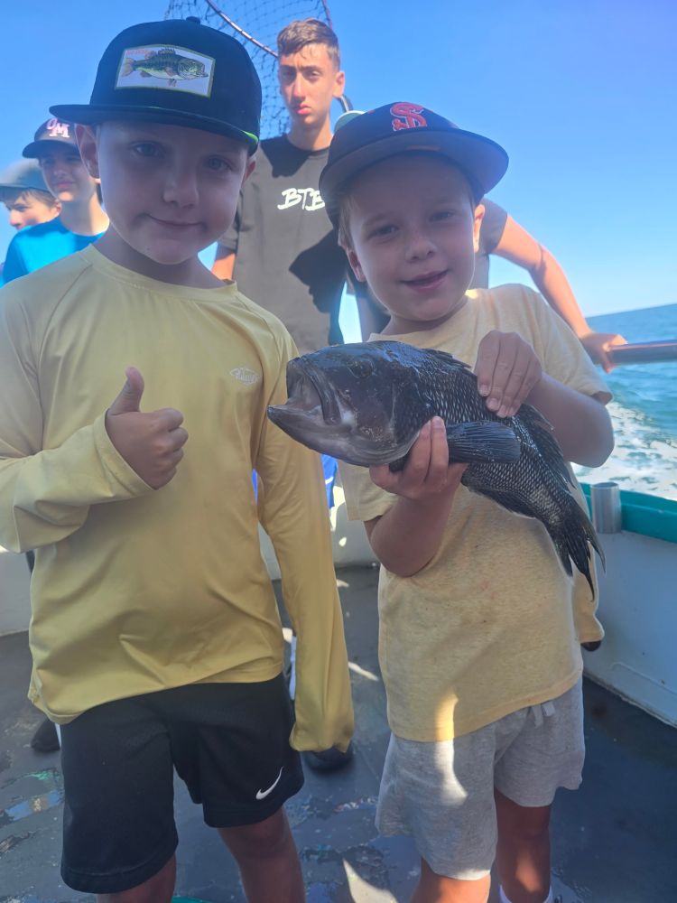 Two boys on a boat, one holding a fish, with ocean in background.