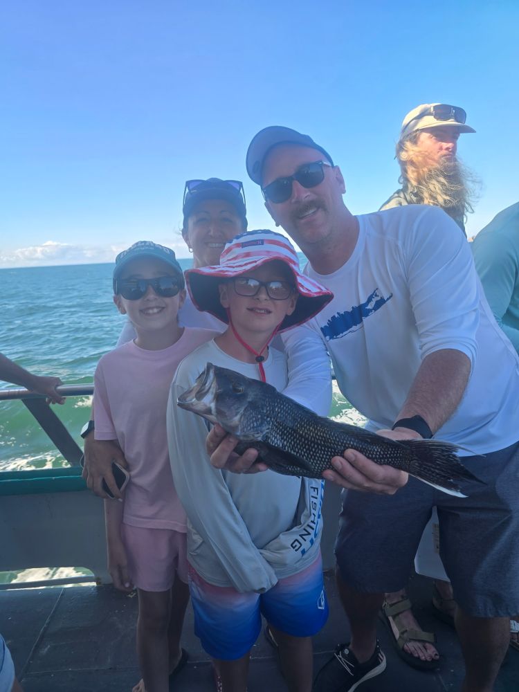 Group on a boat holding a fish, with ocean and blue sky in the background.