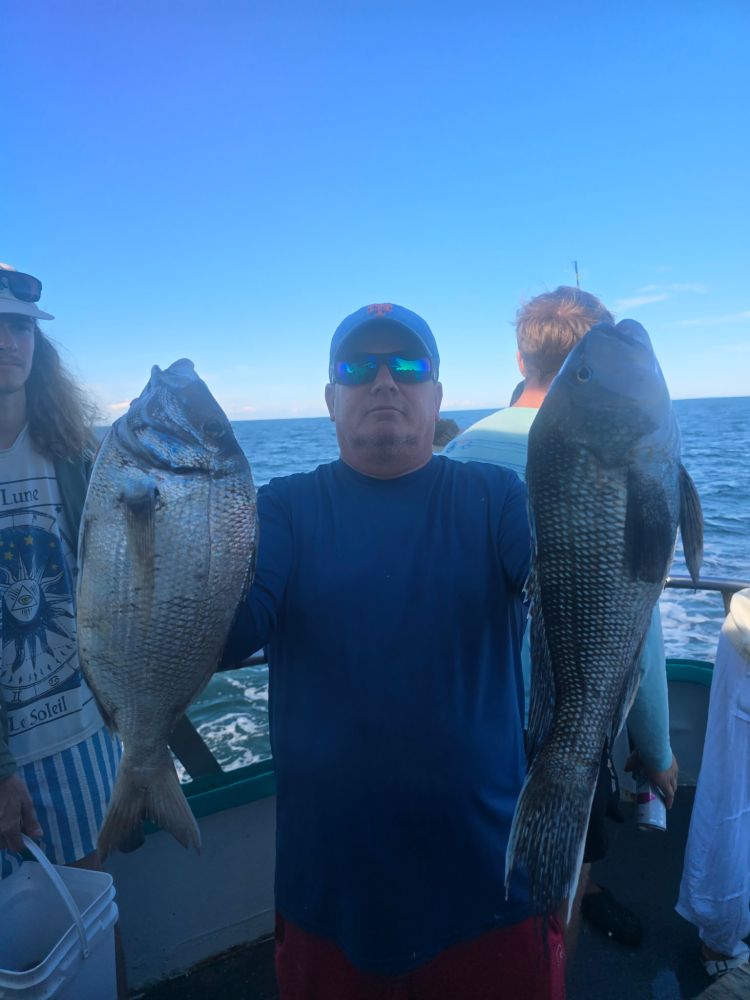 Man holding two large fish on a boat with ocean background.