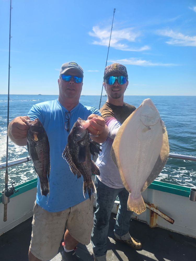 Two men on a boat holding caught fish against ocean backdrop.