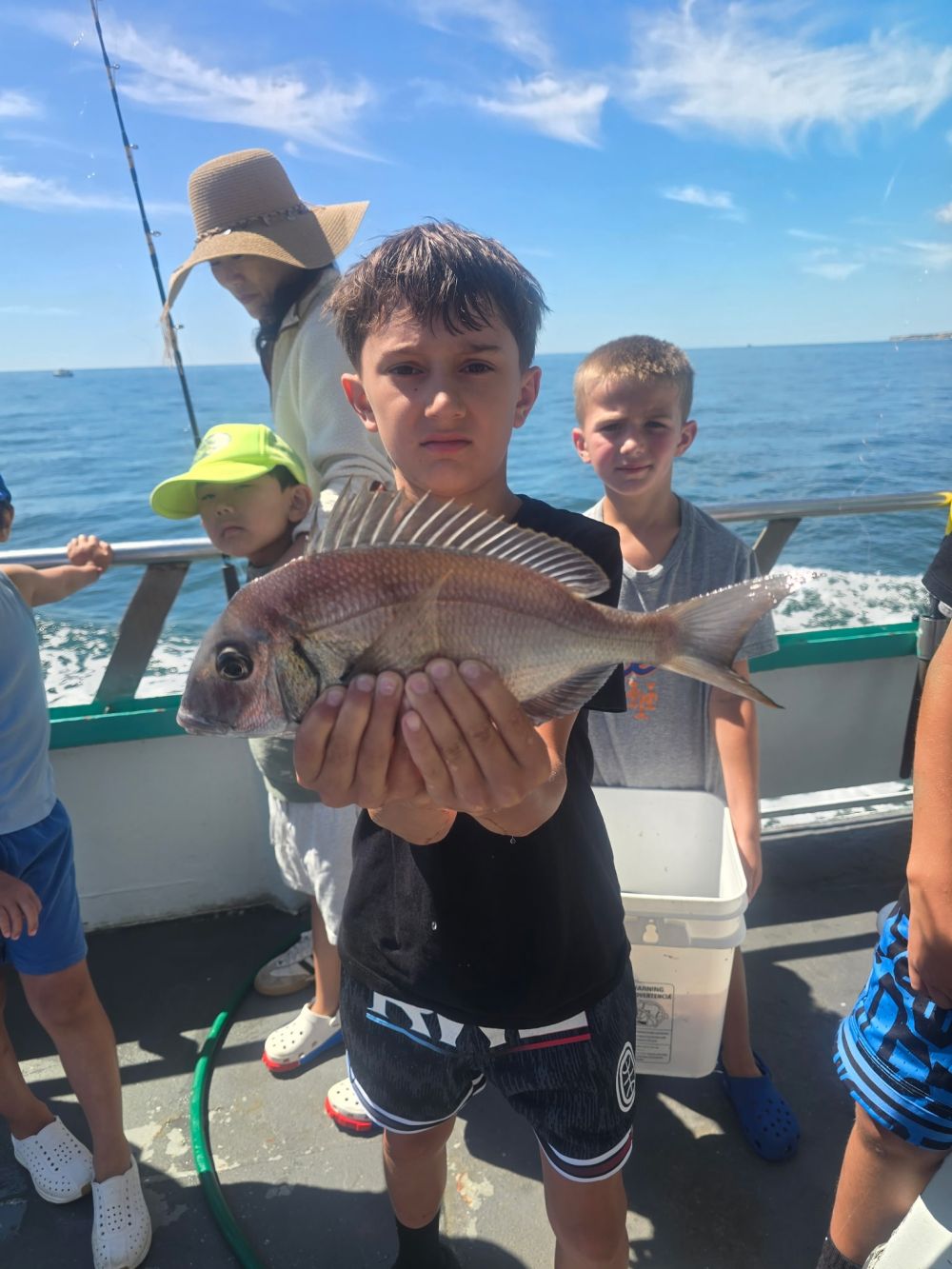 Boy holding a fish on a boat with friends in the background.