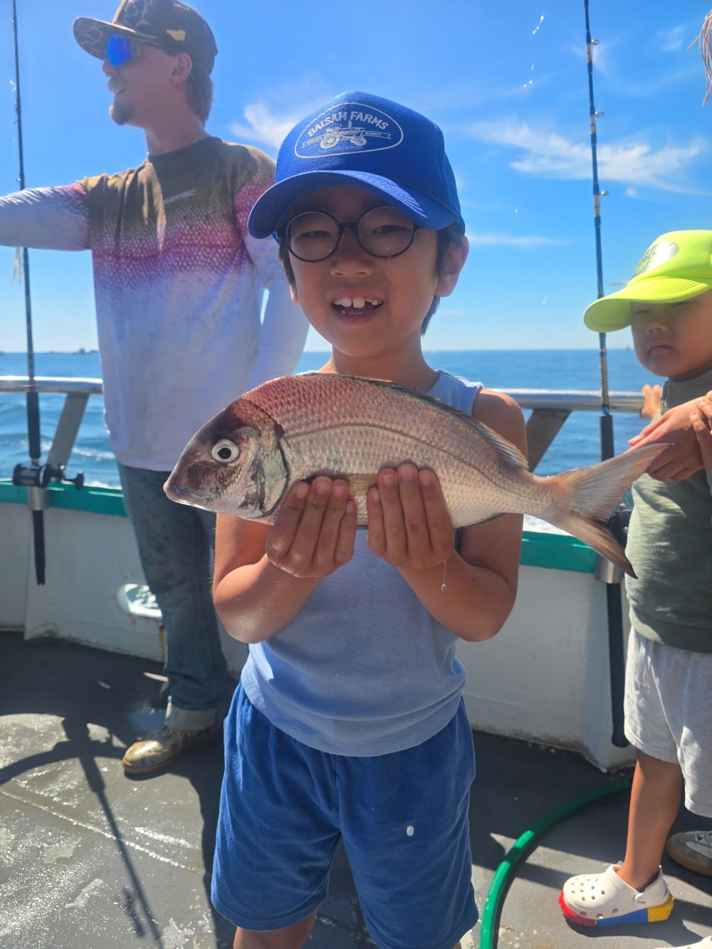 Child holding fish on boat, smiling with others nearby.