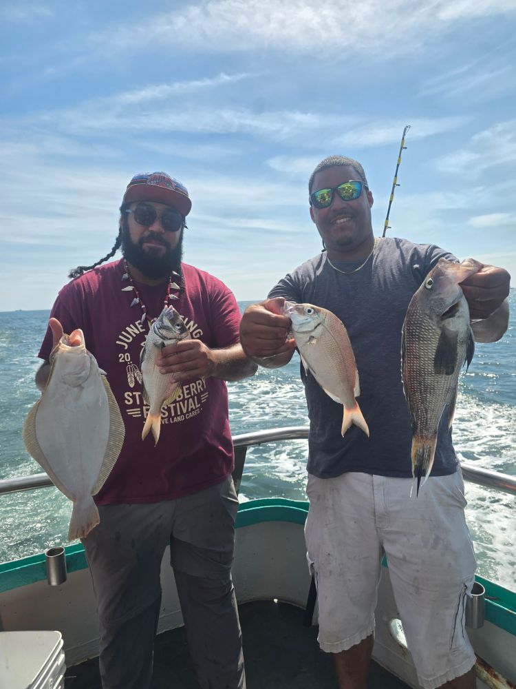 Two men on a boat holding fish they caught under a clear sky.
