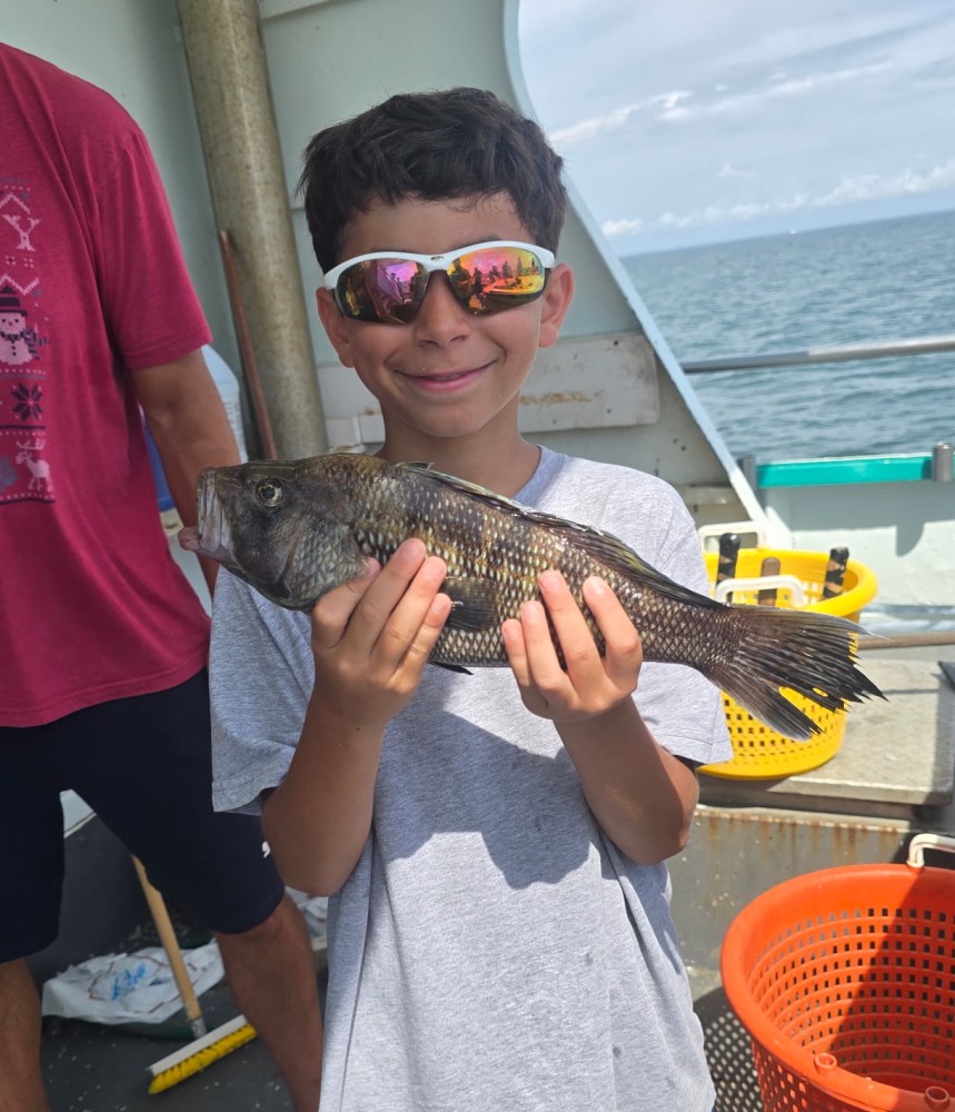 Child smiling and holding a fish on a boat, wearing sunglasses.