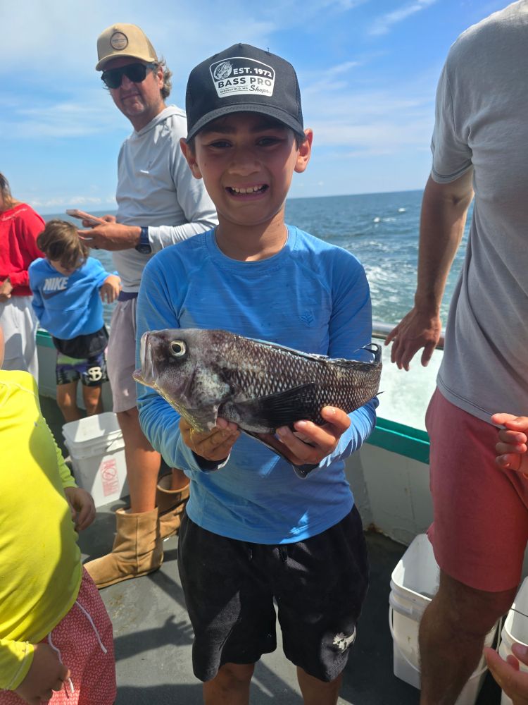 Smiling boy in blue holds a fish on a boat with people in the background.
