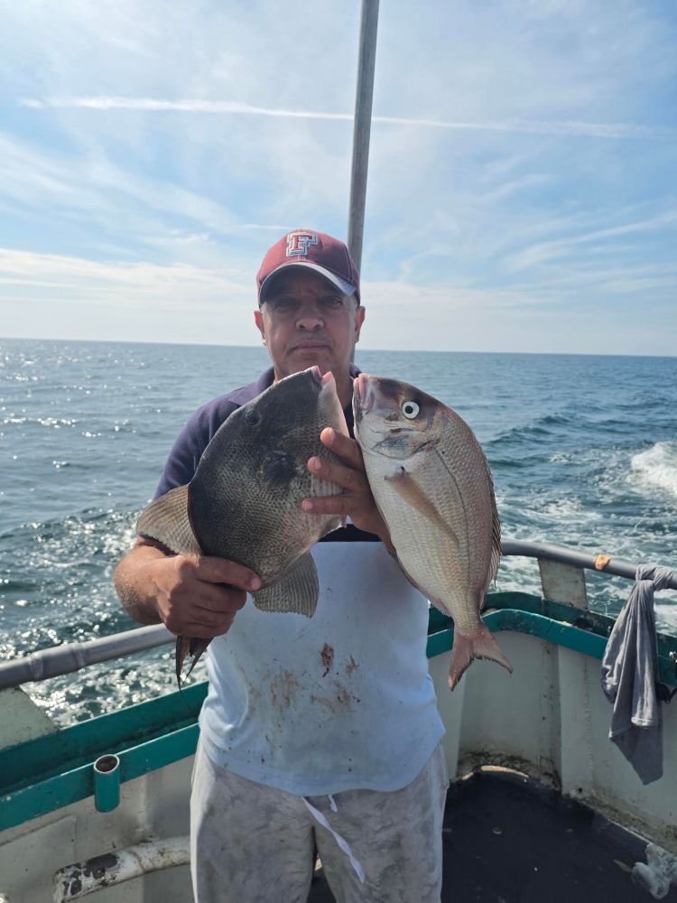 Man on boat holding two fish, ocean background.