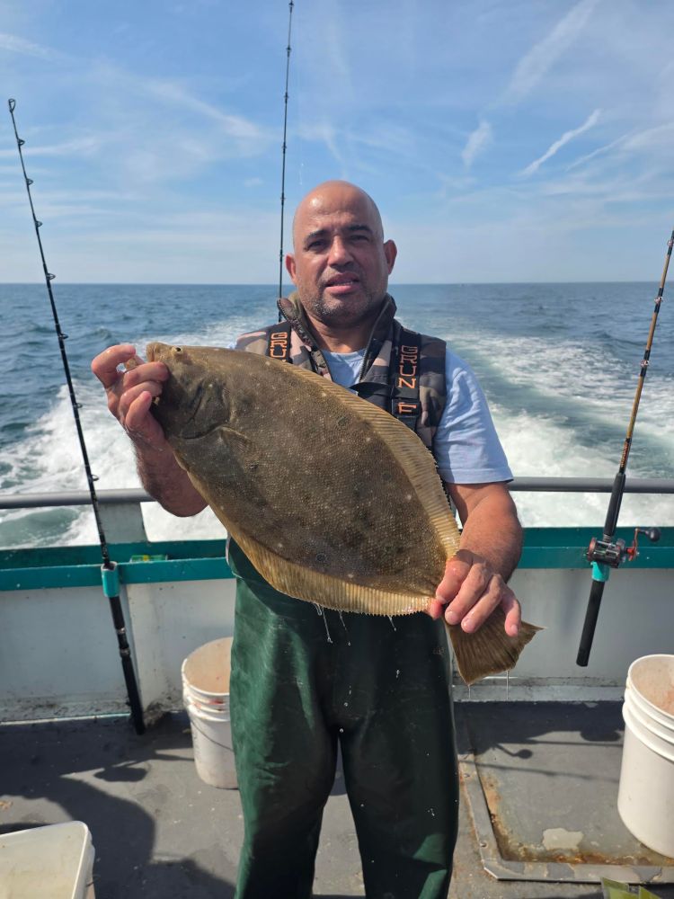 Man holding a large fish on a boat with ocean in the background.